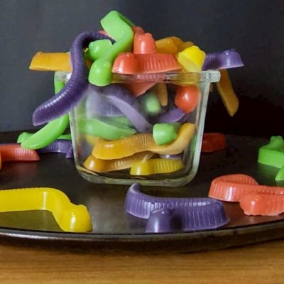 Colorful gummy worms in a glass jar on a black plate.